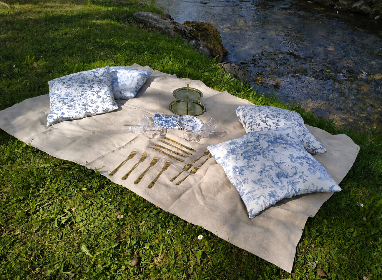 Beige Leinen Picknick-Decke mit vier Kissen im Landhaus-Stil blau-weiß, goldenes Besteck und blau-wei florale Picknickeller und eine golden farbene Etagere